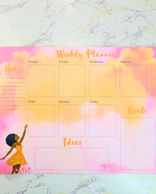A weekly calendar notepad featuring a Black woman reaching for a sky filled with orange clouds against a pink sky. 